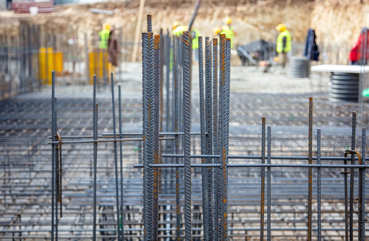 Steel reinforcement rods arranged at a city construction site with workers in safety gear visible in the background under daylight