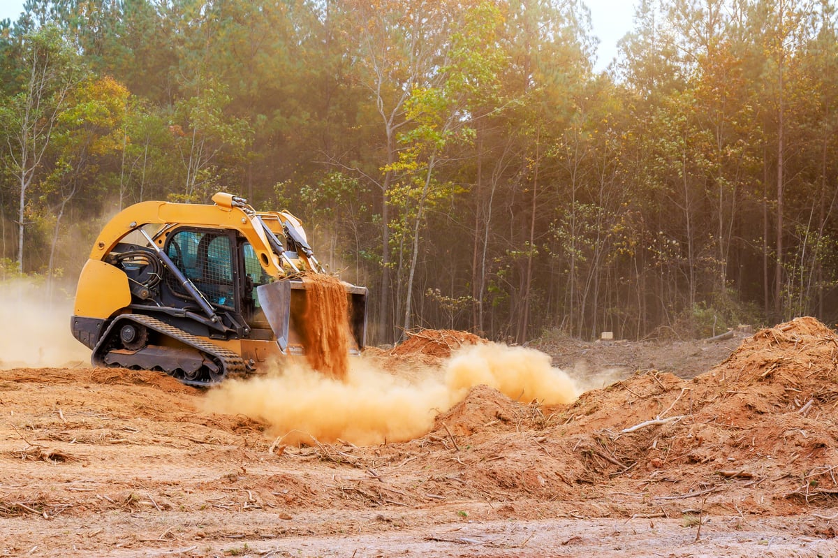 Yellow skid steer works on construction site, moving dirt clearing a site